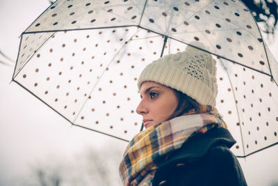 Young woman looking away while holding umbrella in city