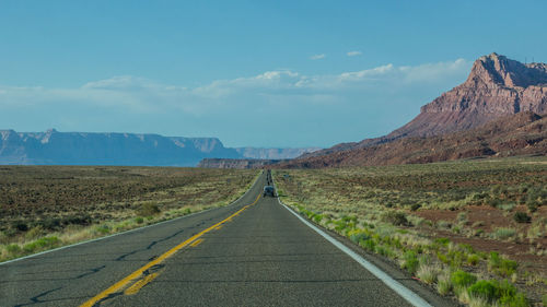 Road leading towards mountains against blue sky