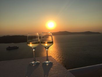 Wineglasses at beach against sky during sunset