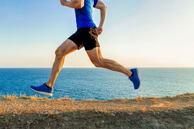 Man mature runner running mountain path in background of sea and sky