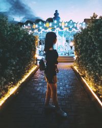 Full length rear view of woman walking on footpath at night