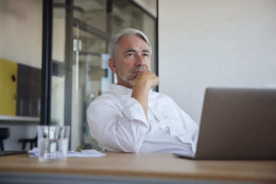 Mature businessman with laptop on table contemplating in office