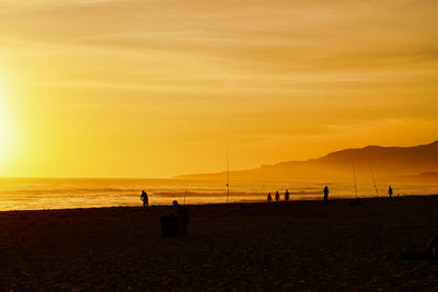 Silhouette people on beach against sky during sunset