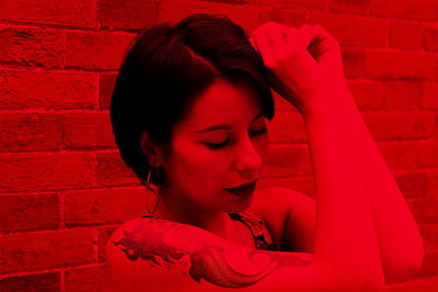 Young woman with tattoos posing against wall with red color