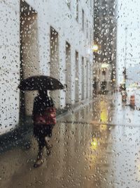 Woman walking on sidewalk seen through wet window during rainy season