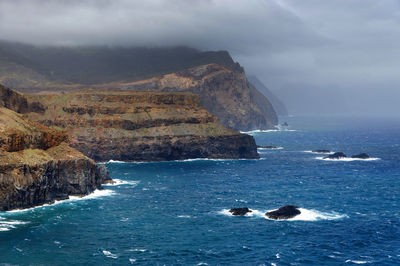 High angle view of rocky coastal feature against clouds