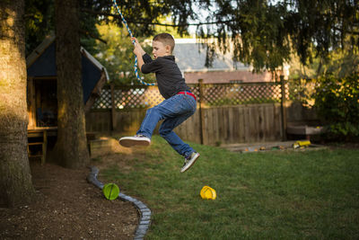 A small boy swings on a rope in his back yard