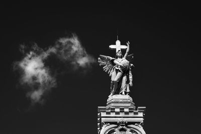 Low angle view of angel statue at cemetery against sky