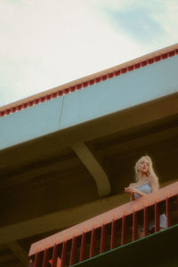 Low angle view of woman looking at railing against sky