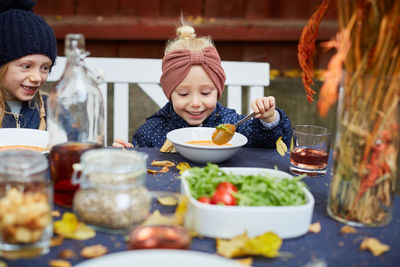 Smiling girl having vegetarian soup while sitting by female sibling at table