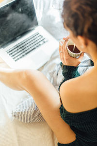 High angle view of woman having coffee while using laptop on bed at home