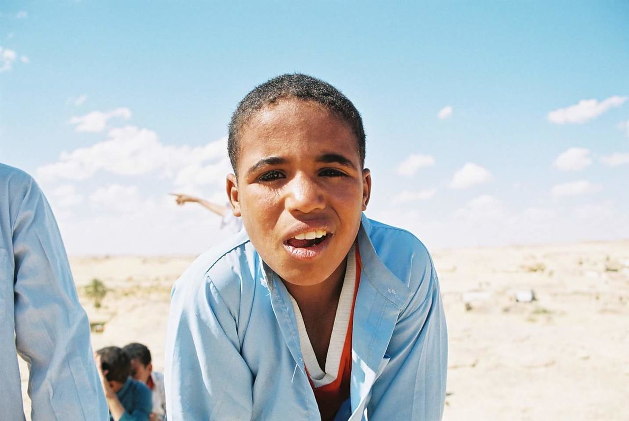 PORTRAIT OF BOY STANDING ON BEACH AGAINST SKY