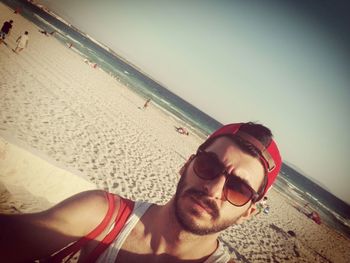 Portrait of young man wearing sunglasses at beach against sky