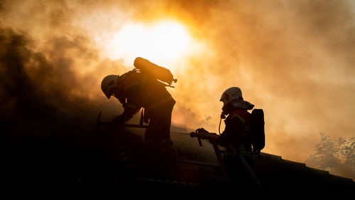 Silhouette firefighters against sky during sunset
