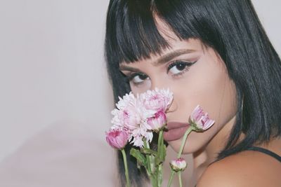 Close-up portrait of beautiful woman with pink flowers against white wall