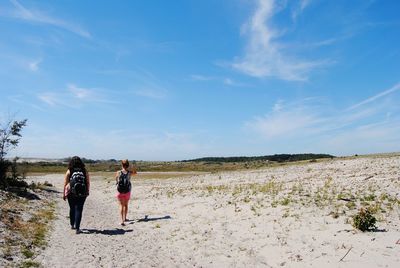 Rear view of women walking on sand against blue sky