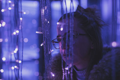Young woman by illuminated string lights 