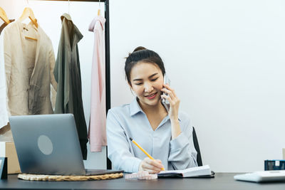 Smiling young woman using phone while sitting on table