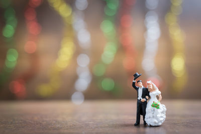 Close-up of married couple figurines on table against illuminated lights