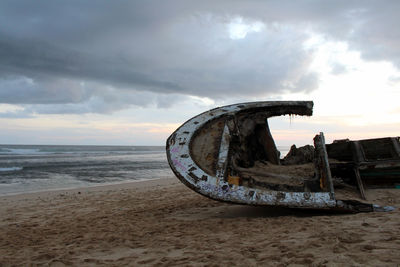 Abandoned boat on beach against sky during sunset