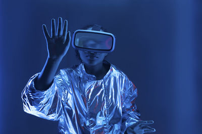 Young woman in virtual reality simulator gesturing against blue background