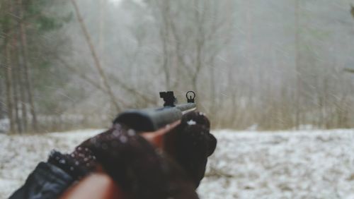 Close-up of hand using a gun against trees