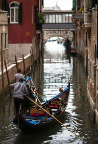 Men sailing gondolas on canal in city