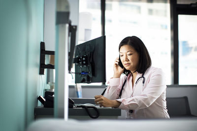 Female doctor using smart phone computer desk in clinic