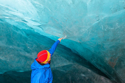 Man touching turquoise glacier at cave