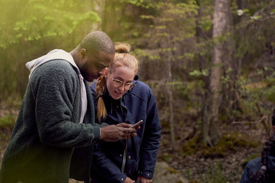 Man showing smart phone while standing with daughter in forest