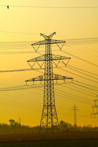 Low angle view of electricity pylon against sky during sunset