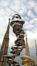 Low angle view of sculpture and milan cathedral against cloudy sky in city