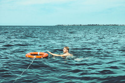 Man and life ring in sea against sky