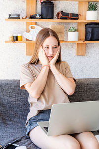 Young woman using mobile phone while sitting in laptop