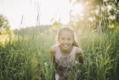 Portrait of happy girl playing in grass during sunny day