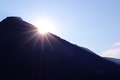 Low angle view of sunlight streaming through silhouette mountain range