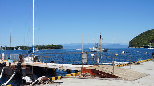 Sailboats moored at harbor against clear blue sky