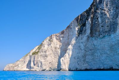 Rock formations by sea against clear blue sky