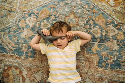 Overhead of toddler laying on carpet with a dinosaur covering face