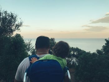 Rear view of couple sitting by sea against sky