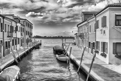 Boats moored in canal by buildings against sky