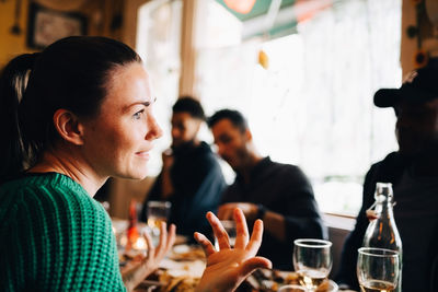 Smiling young woman gesturing while sitting in restaurant during brunch party