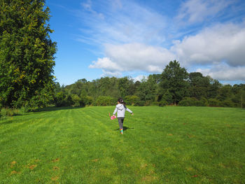 Full length of  young girl  running on the grass field against sky