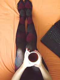 Low section of woman sitting with black coffee and laptop on bed