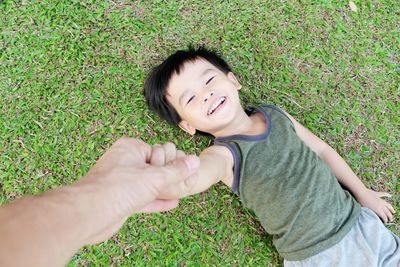 Little asian boy laying on the lawn happily and blurry hand of father takes care.