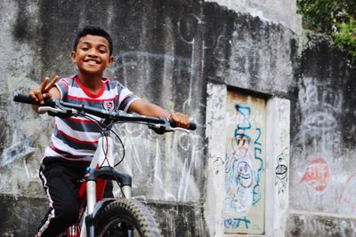 Portrait of smiling boy riding bicycle against graffiti wall