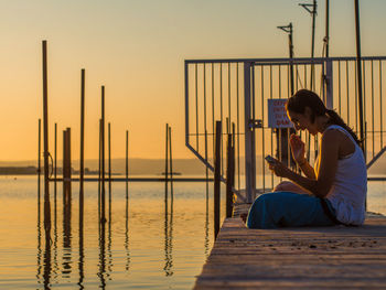 Side view of woman sitting on lake jetty