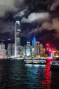 Illuminated buildings by river against sky at night