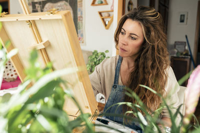 Concentrated woman in front of easel painting at home