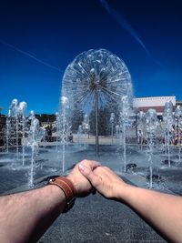 Low angle view of hand against illuminated city against blue sky
